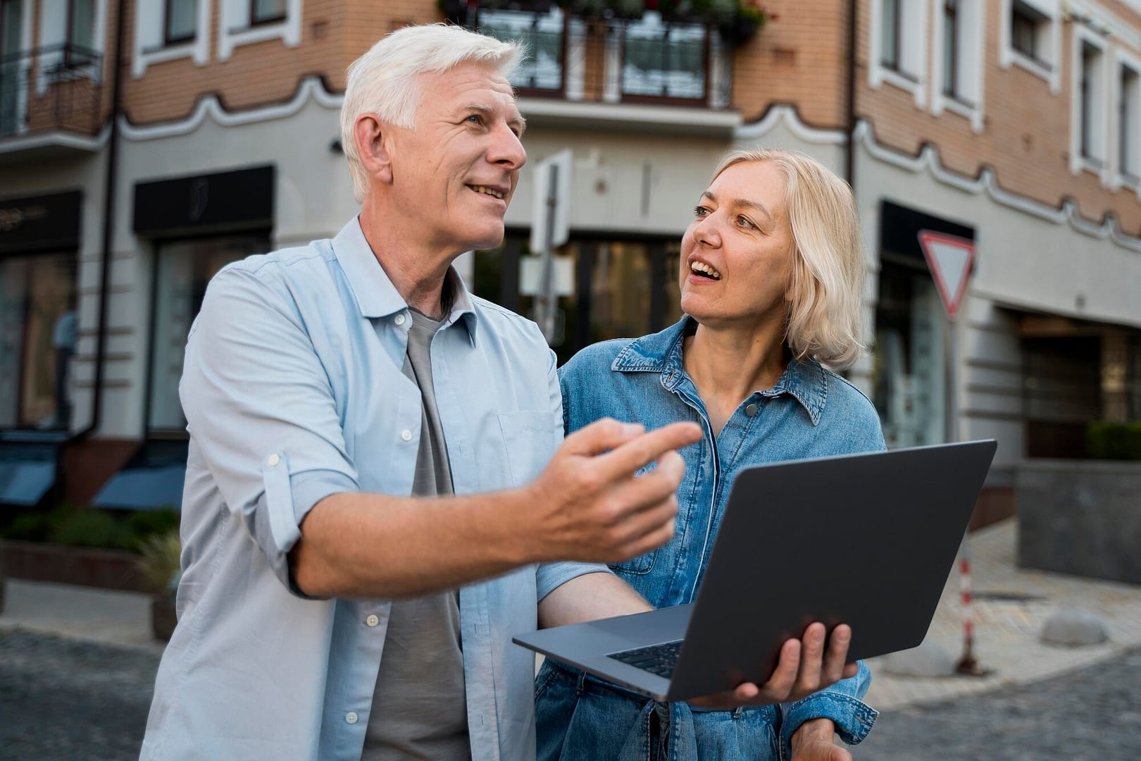 Middle aged couple holding laptop on street looking at a property